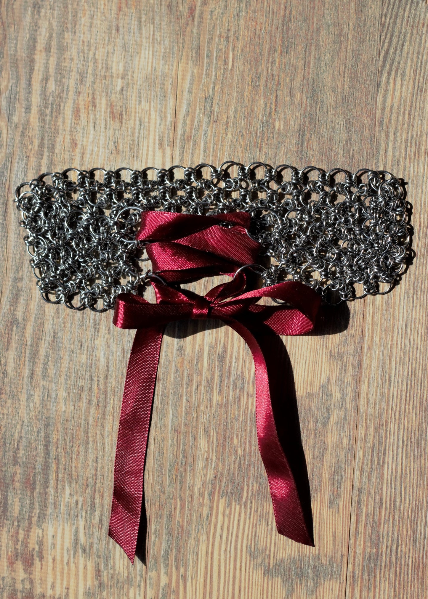 Chainmail choker z bordową wstążką  w sylu romantic lolita, położony na drewnianej powierzchni.