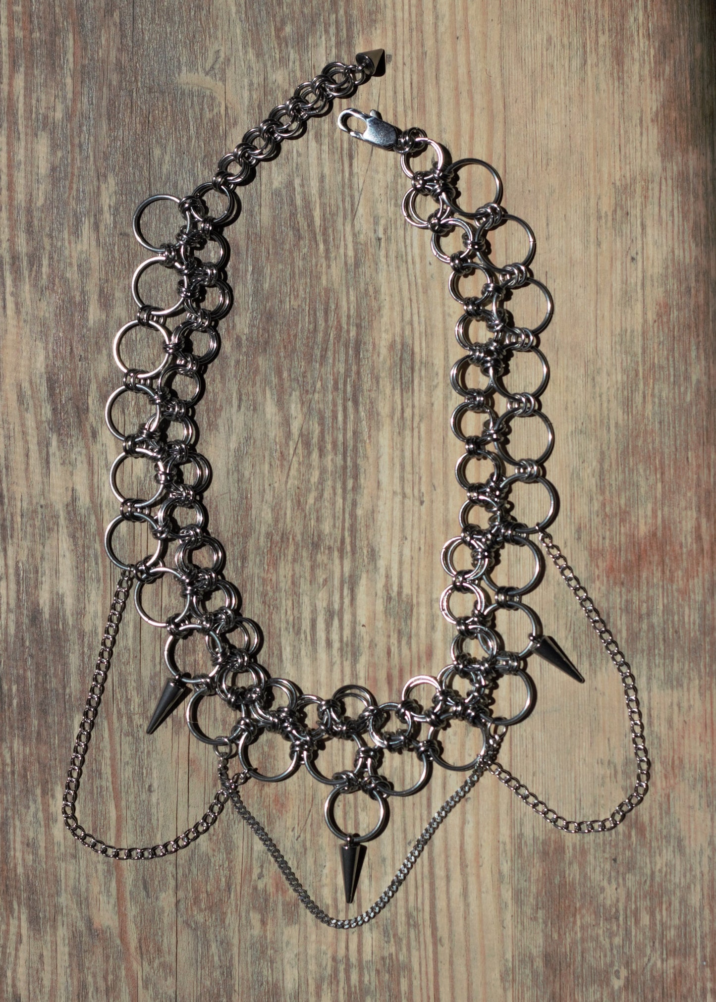 Ręcznie robiony choker chainmail w stylu punk, industrial. Położony na drewnianej powierzchni.