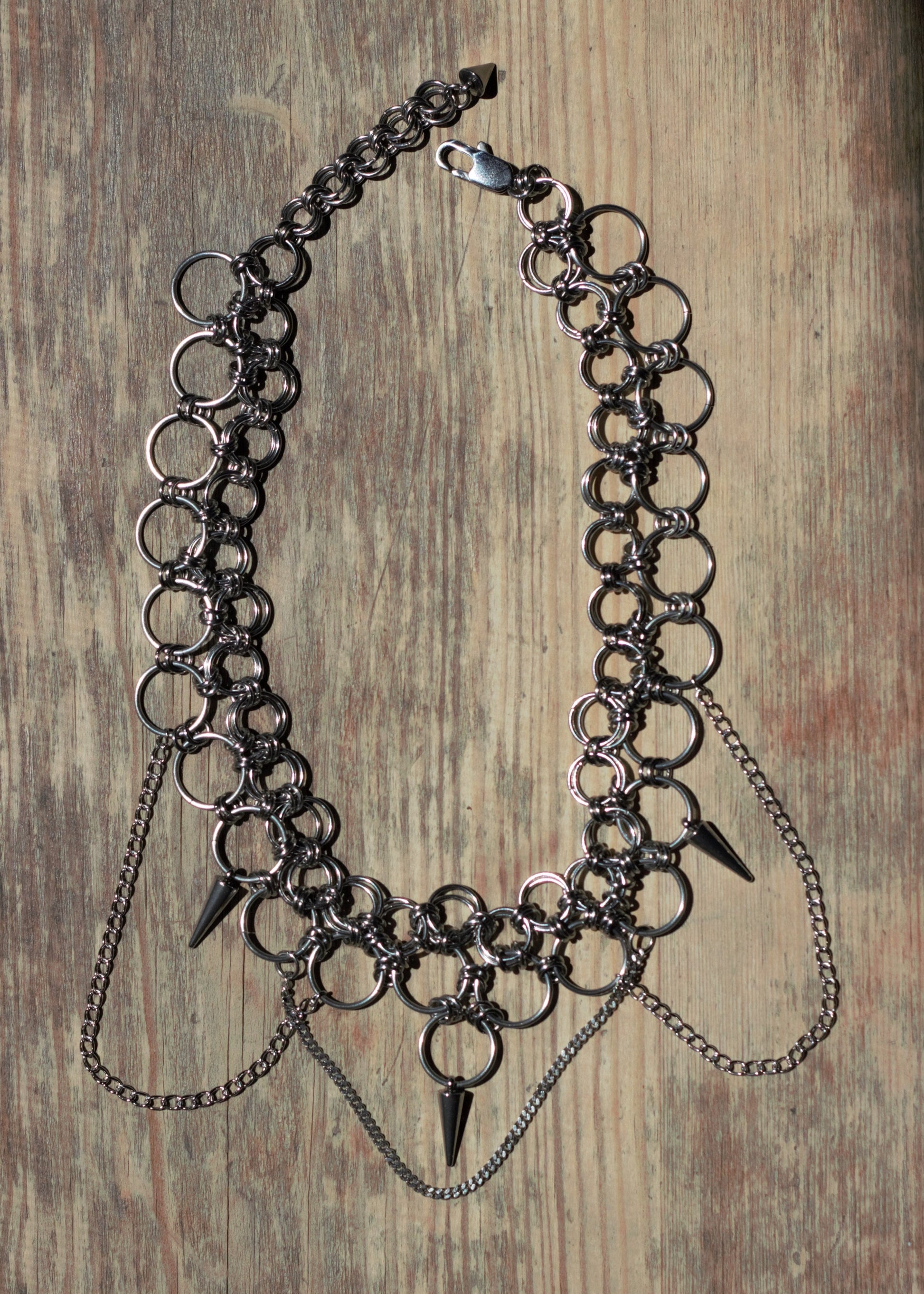 Ręcznie robiony choker chainmail w stylu punk, industrial. Położony na drewnianej powierzchni.