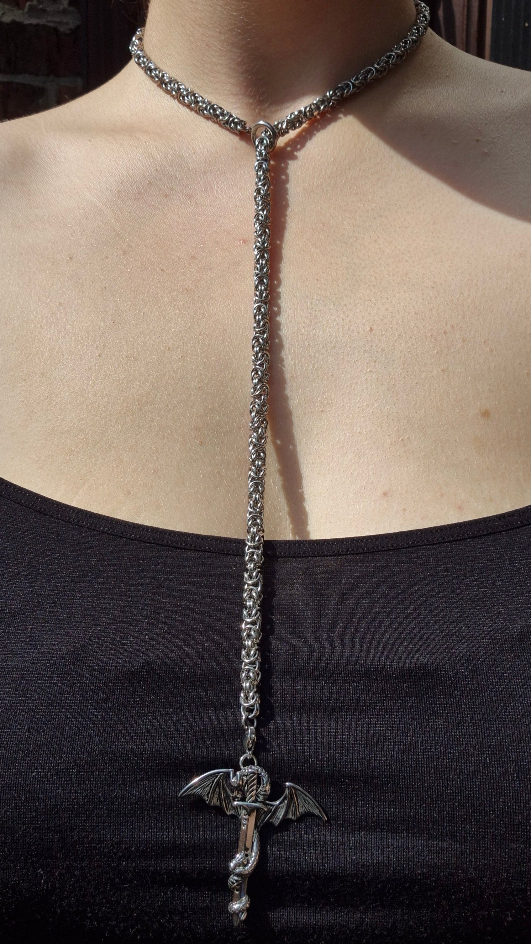 Gotycki naszyjnik z motywem smoka i miecza na masywnym łańcuszku chainmail, noszony jako klasyczny naszyjnik.